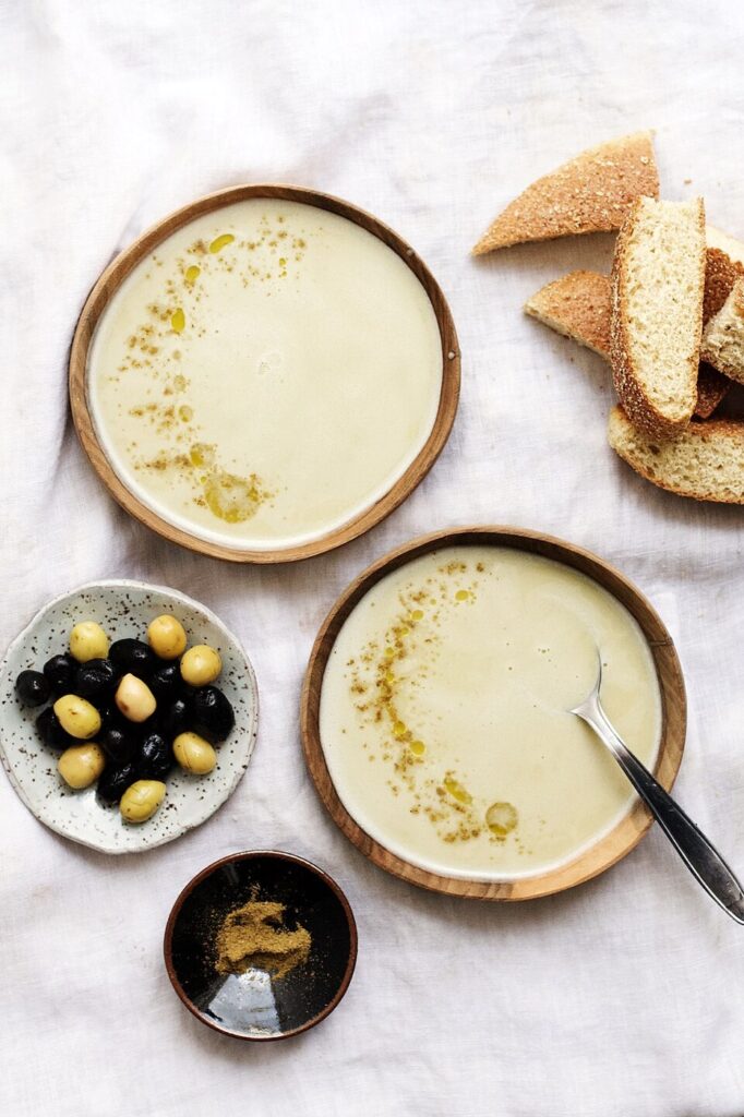 Deux bols de bissara, avec olives, épices et pain à côté.