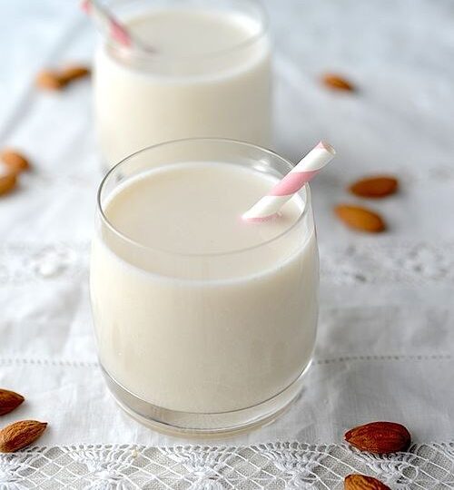 Deux verres de boisson d’amande blanche avec des amandes à côté.