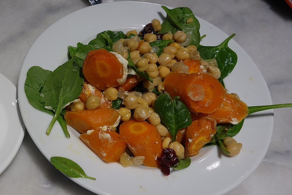 Assiette de carottes en rondelles avec légumineuses et feuilles vertes.