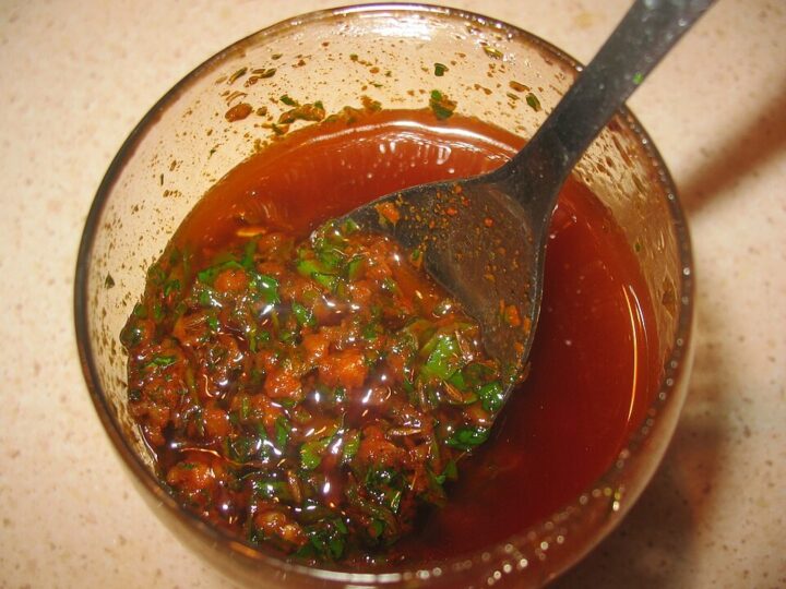 Bol de chermoula rouge avec herbes hachées et une cuillère.
