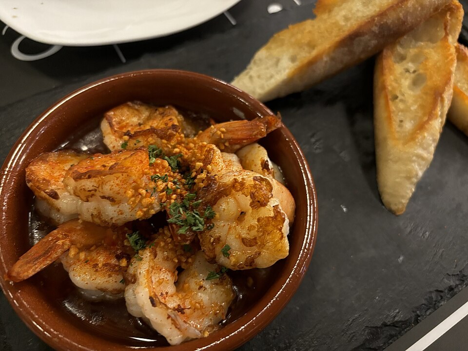 Crevettes à l’ail dans un petit plat, avec herbes et pain à côté.