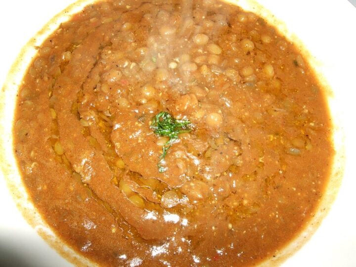 Assiette creuse de soupe de lentilles avec une garniture verte.
