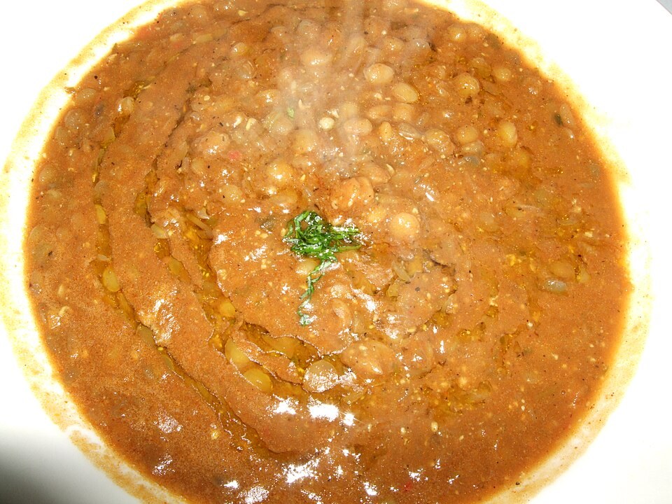 Assiette creuse de soupe de lentilles avec une garniture verte.