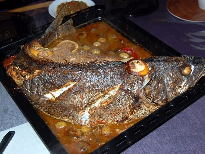 Poisson entier cuit au four dans un plat avec sauce, citron et olives.
