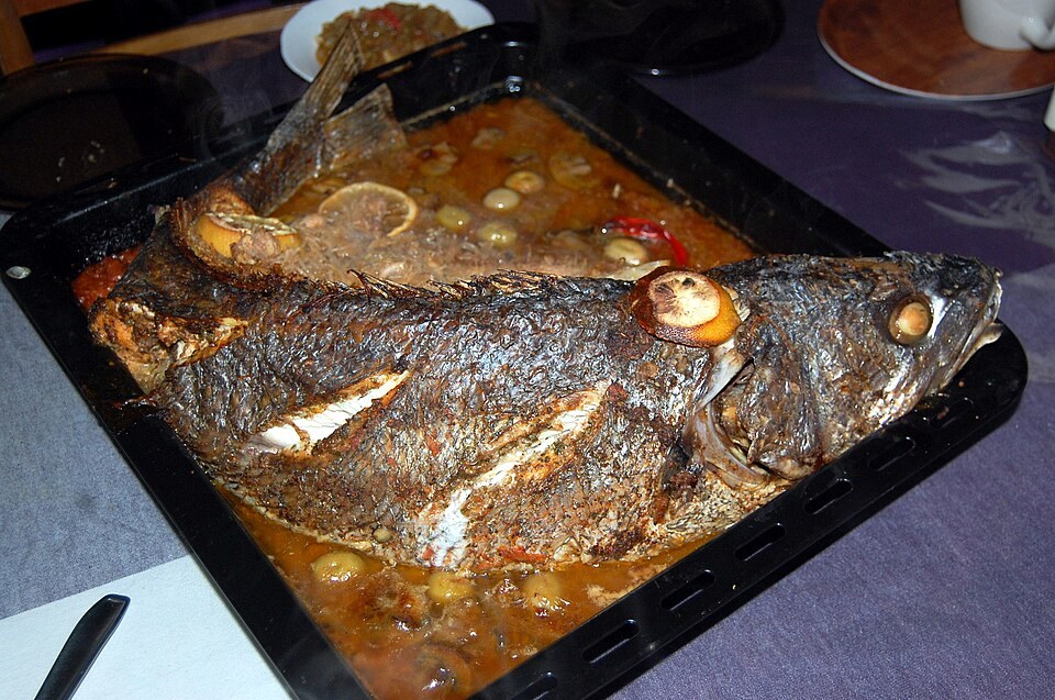 Poisson entier cuit au four dans un plat avec sauce, citron et olives.