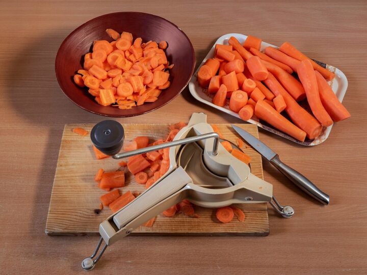 Carottes épluchées et découpées, avec un coupe-légumes sur une planche.